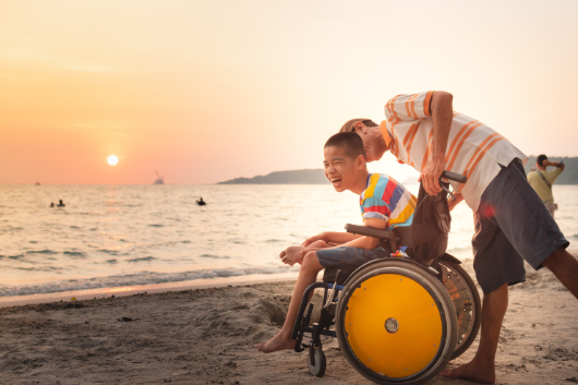 man with his son in a wheelchair at the beach