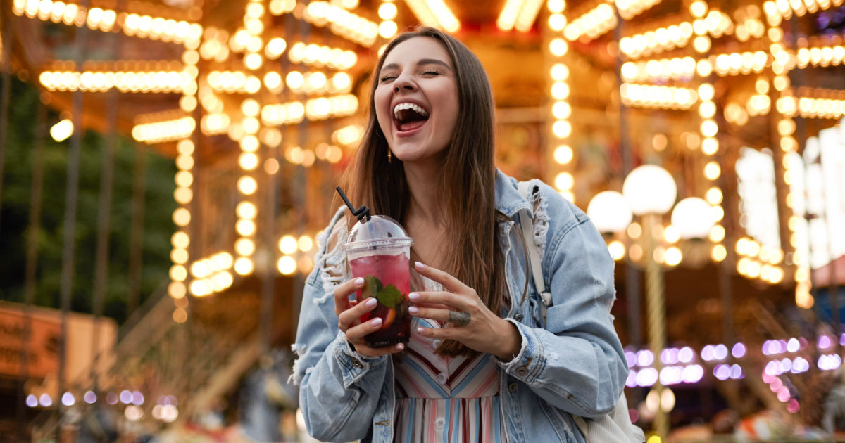 Young woman having refreshing drink and laughing at amusement park