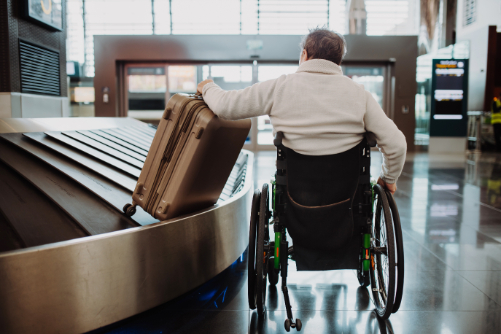 man in wheelchair getting luggage from baggage claim at airport