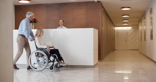 man walking woman in wheelchair up to lobby desk at a hotel