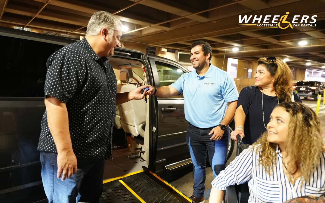 Wheelers Accessible Van Rentals employee handing over van keys to a smiling customer at a Tampa parking garage, with a woman in a wheelchair nearby, showcasing wheelchair-accessible transportation services in Tampa, Florida.