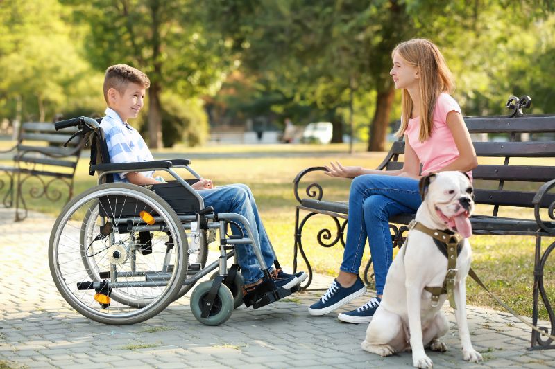 Boy in Wheelchair Talking to Girl Sitting on Park Bench