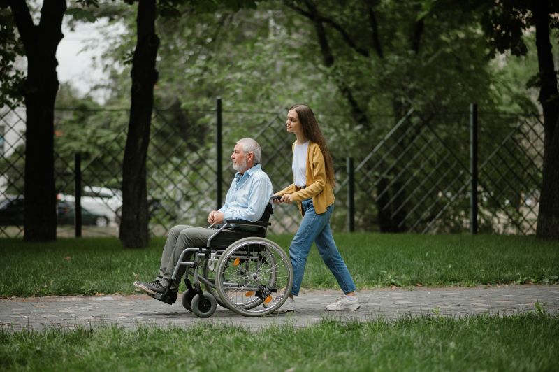 Daughter walking disabled man in Wheelchair