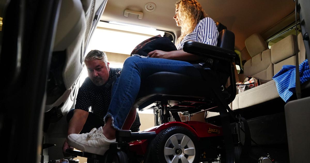 Woman in wheelchair being secured by driver in accessible van